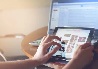 Personne utilisant une tablette devant un ordinateur portable sur une table en bois.